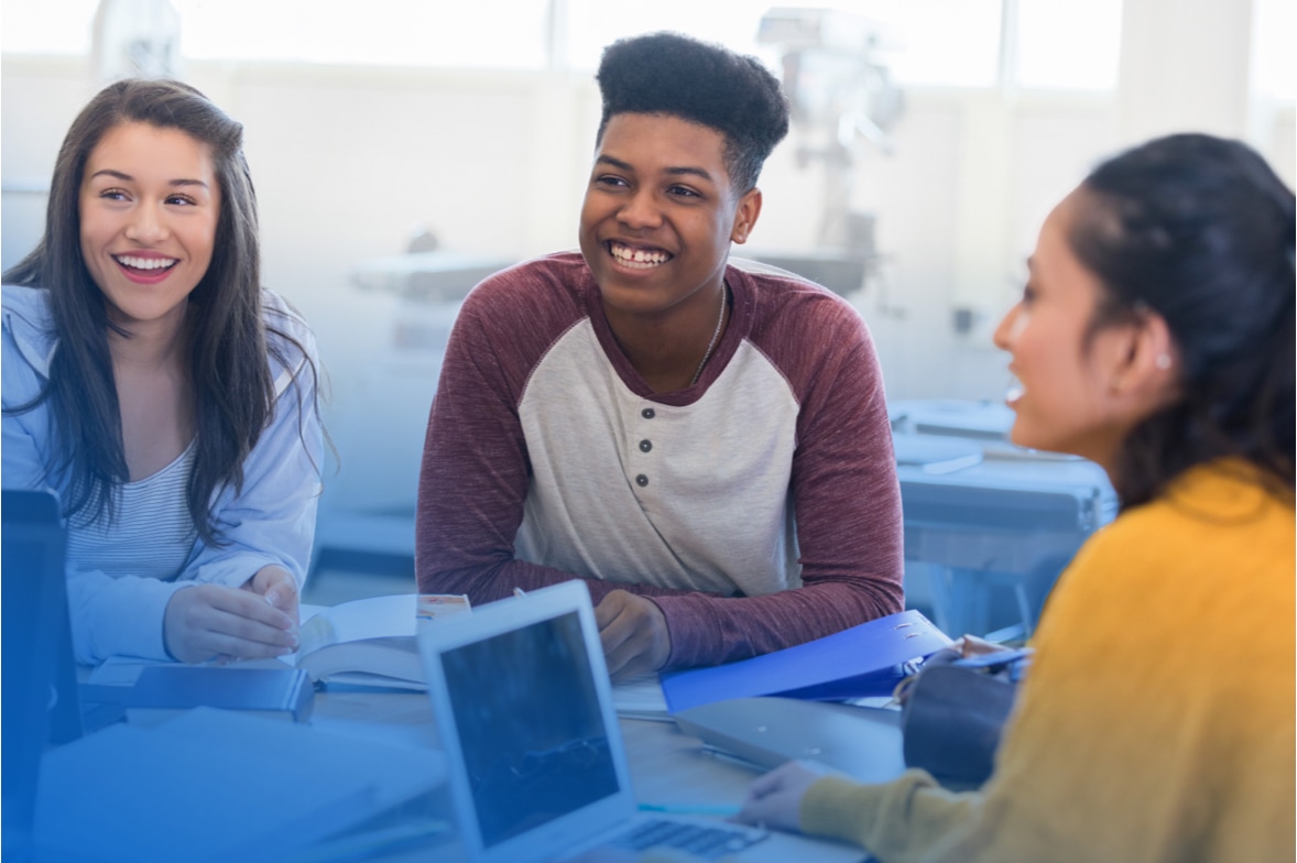 three smiling students seated in meeting with laptop computer