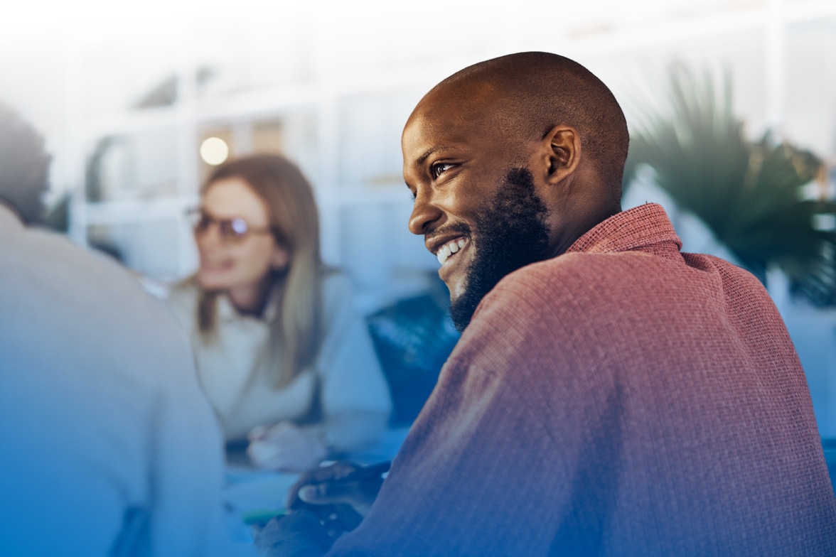 Man smiling and engaged in conversation, with other people blurred in background.