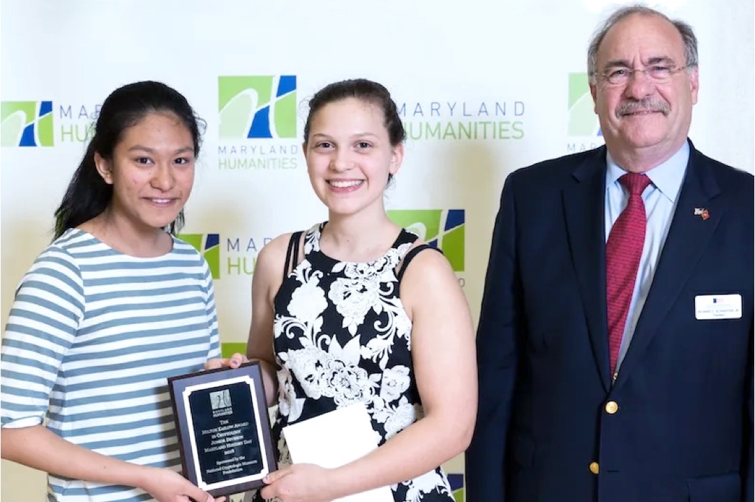 two students next to man hold up award for cryptology achievement